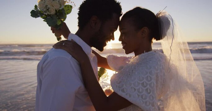 African american couple in love getting married, looking at each other on the beach at sunset