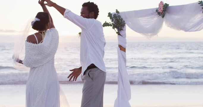 African american couple in love getting married, smiling and dancing on the beach at sunset