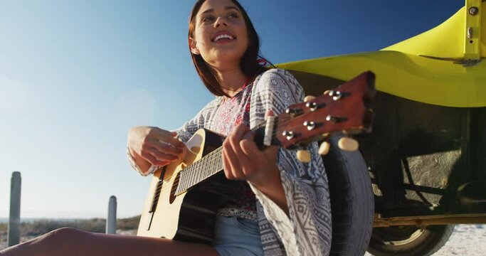 Happy caucasian woman sitting in beach buggy by the sea playing guitar
