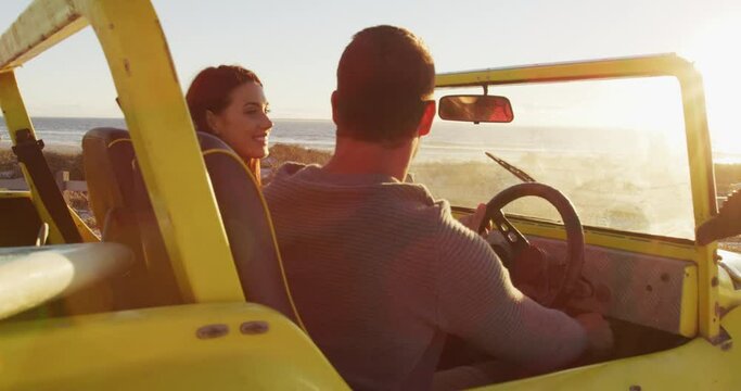 Happy caucasian couple sitting in beach buggy by the sea talking