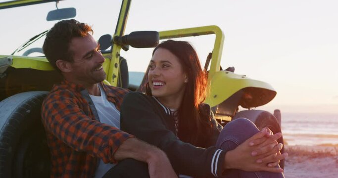 Happy caucasian couple sitting beside beach buggy by the sea talking hugging