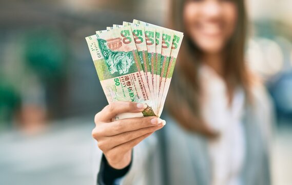 Young latin businesswoman smiling happy holding hong kong dollars at the city.
