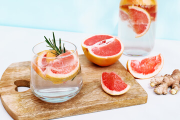 Summer cocktail with grapefruit and rosemary and juicy slices citrus fruits. Fresh healthy grapefruit beverage on sunlight with shadows. Creative drink on blue pastel background.