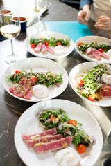 Group of plates with appetizing smoked meat, vegetable stew or salad and sourcream standing close to each other on large served kitchen table