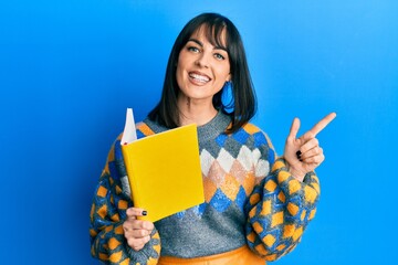Young hispanic woman reading book smiling happy pointing with hand and finger to the side