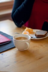 Woman sitting at the wooden kitchen table having her morning coffee with orange fruit and sweet homemade bread with some paperwork nearby