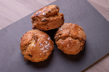 Three freshly baked fruit scones on slate plate .