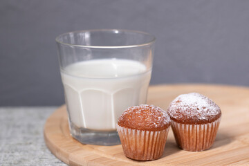 two little cupcakes or muffins in powdered sugar near a glass of milk. healthy breakfast. snack or lunch