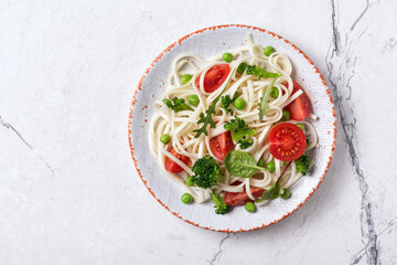 A dish of Asian cuisine. Udon noodles with cherry tomatoes, broccoli and green pea