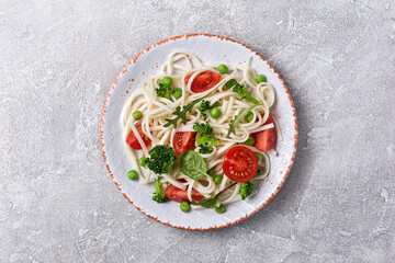 A dish of Asian cuisine. Udon noodles with cherry tomatoes, broccoli and green pea
