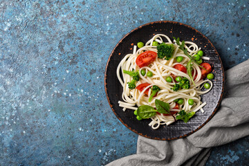 A dish of Asian cuisine. Udon noodles with cherry tomatoes, broccoli and green pea