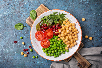 A plate of healthy food: chickpeas with mix of fresh leaves, pomegranate, green peas and cherry tomatoes