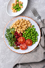 A plate of healthy food: chickpeas with mix of fresh leaves, pomegranate, green peas and cherry tomatoes