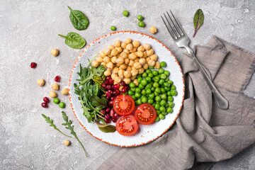 A plate of healthy food: chickpeas with mix of fresh leaves, pomegranate, green peas and cherry tomatoes