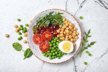 A plate of healthy food: chickpeas with mix of fresh leaves, pomegranate, green peas, cherry tomatoes and boiled egg