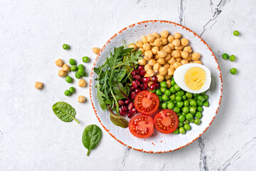 A plate of healthy food: chickpeas with mix of fresh leaves, pomegranate, green peas, cherry tomatoes and boiled egg