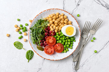 A plate of healthy food: chickpeas with mix of fresh leaves, pomegranate, green peas, cherry tomatoes and boiled egg