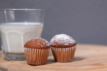 two little cupcakes or muffins in powdered sugar near a glass of milk. healthy breakfast. snack or lunch