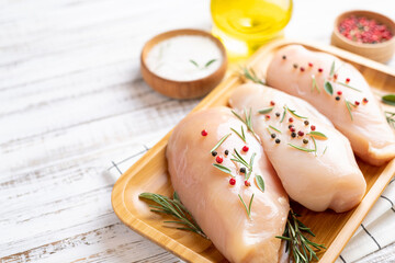 Raw uncooked chicken breasts with spices and herbs on white wooden background, chicken meat with ingredients for cooking. Copy space