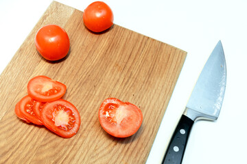 Close up of chopped fresh ripe tomatoes vegetables and knife on a wooden cutting board on white background in a kitchen at home, vegetarian food.