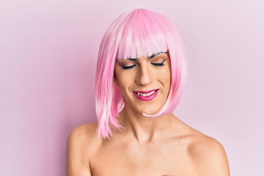 Young man wearing woman make up wearing pink wig looking confident at the camera smiling with crossed arms and hand raised on chin. thinking positive.