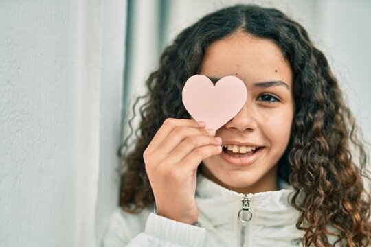 Hispanic teenager girl smiling happy holding heart over eye at the city.