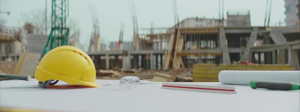 Architectural equipment at construction site. Yellow helmet, engineering diagram blueprint paper and several drawing tools.