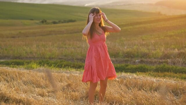 Happy long haired young woman dancing on golden wheat field at sunset.