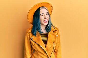 Young modern girl wearing yellow hat and leather jacket winking looking at the camera with sexy...