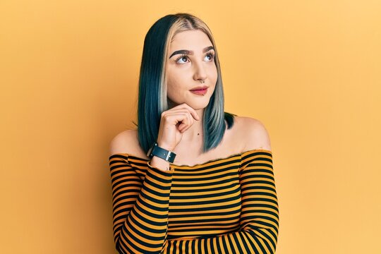 Young modern girl wearing casual striped shirt thinking concentrated about doubt with finger on chin and looking up wondering