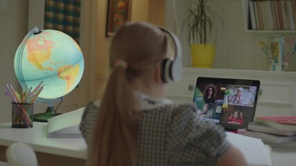 Schoolgirl learning with online school teacher and pupils on laptop screen. Girl in headphones sitting at the desk and studying by internet. Remote learning and home schooling process. - Powered by Adobe