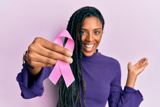 African american woman holding pink cancer ribbon celebrating achievement with happy smile and winner expression with raised hand