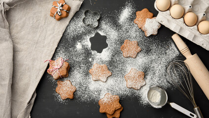 Obraz na płótnie Canvas Star shaped baked gingerbread cookies sprinkled with powdered sugar on a black table