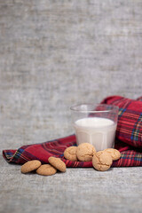 glass of milk near almond amaretti cookies on plaid red fabric tablecloth. healthy breakfast snack