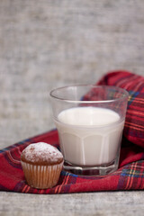 cupcake or muffin in powdered sugar near a glass of milk on plaid red fabric tablecloth. healthy breakfast. snack or lunch