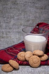 glass of milk near almond amaretti cookies on plaid red fabric tablecloth. healthy breakfast snack