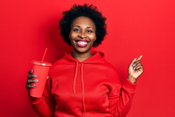 Young african american woman drinking glass of cola beverage smiling happy pointing with hand and finger to the side