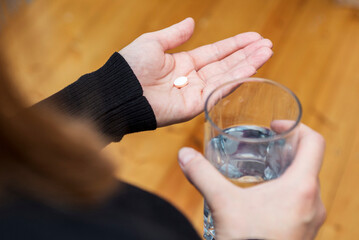 Close up of young woman holds pill and glass of water. A woman takes the pill