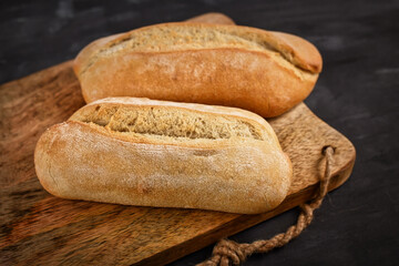 Rustic bread rolls on wooden cutting board on dark table