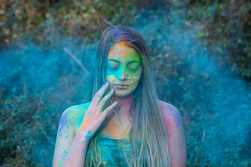 Obraz na płótnie Canvas Young attractive woman at the Holi color festival of paints in park. Having fun outdoors. Multi Colored powder colors the face. Close Up portrait, people. Copy Space.