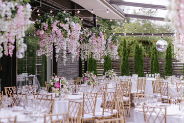 Gold chairs and tables decorated with natural pink and green flowers, candles and gold frames. Hanging flower beds and light bulbs
Wedding decoration and decor, floristic concept