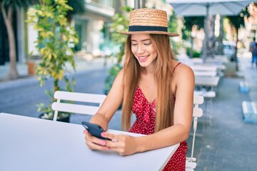 Fototapeta premium Young caucasian tourist girl smiling happy using smartphone at coffee shop terrace