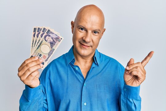 Middle age bald man holding 5000 japanese yen banknotes smiling happy pointing with hand and finger to the side