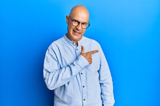 Middle age bald man wearing casual clothes and glasses cheerful with a smile of face pointing with hand and finger up to the side with happy and natural expression on face
