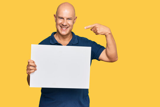Middle age bald man holding blank empty banner pointing finger to one self smiling happy and proud