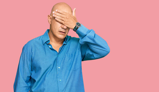 Middle age bald man wearing casual clothes covering eyes with hand, looking serious and sad. sightless, hiding and rejection concept