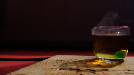 Isolated linden tea cup made of glass and there is green mentholated sweat and candy. Fully linden tea filled glass pot existing on wooden plate and red carpet.