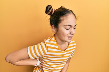 Beautiful brunette little girl wearing casual striped t shirt suffering of backache, touching back with hand, muscular pain