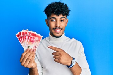 Young arab handsome man holding 20 israel shekels banknotes smiling happy pointing with hand and...
