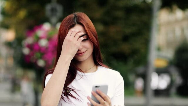 Portrait of Beautiful young woman texting message on smartphone on city street in slow motion
